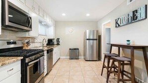 A modern kitchen with white cabinets, a stainless steel refrigerator, a microwave, and a stove.