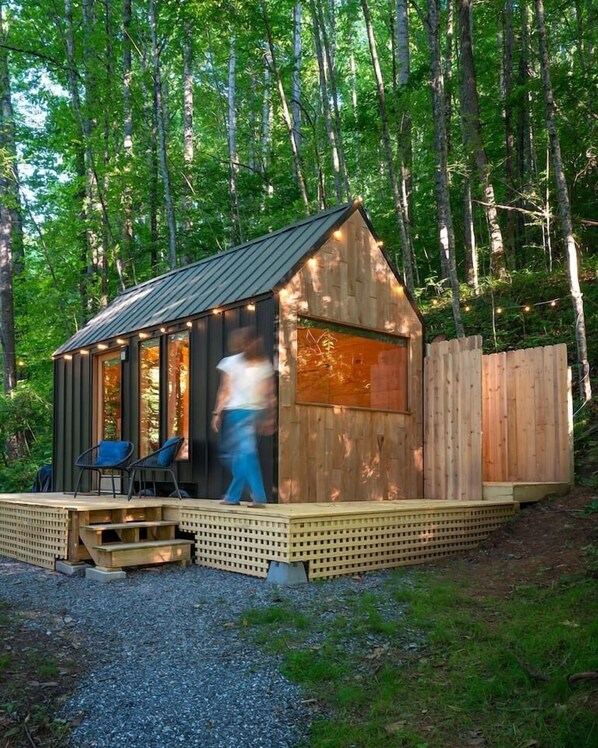 A wooden cabin with a metal roof, a porch with two chairs, and a wooden deck.