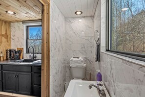 Une salle de bain avec un mur en marbre, un lavabo, des toilettes et une fenêtre donnant sur des arbres.