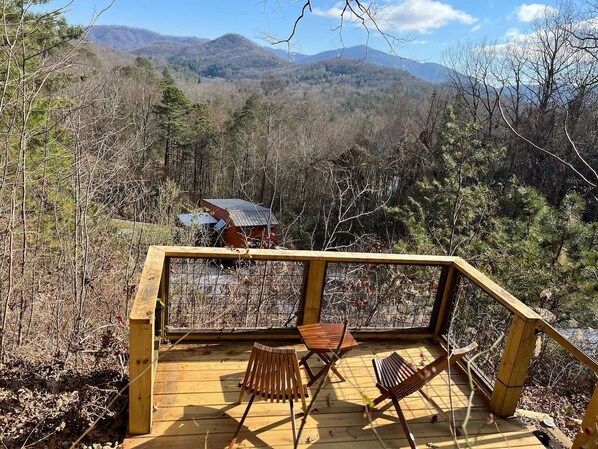 A wooden deck with chairs overlooking a forested area and a cabin in the background.