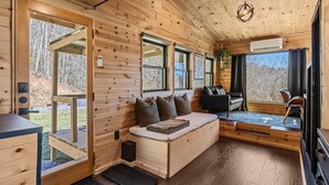 A cozy cabin interior with a wooden interior, a sofa with cushions, a dining table, and a kitchen area.