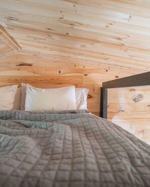 Una habitación tipo cabaña de madera con una cama, almohadas y una ventana.