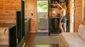 A cozy cabin with a wooden interior, a bed, a kitchenette, and a large window.
