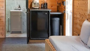 A compact kitchen with a microwave, coffee maker, and shelves with glassware.
