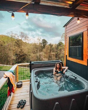 Un bain à remous sur une terrasse en bois, avec vue sur les arbres et les collines.