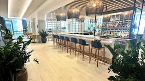Uma área de bar moderna com um balcão longo, vários bancos altos e luminárias pendentes.