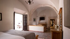 A bedroom with a large bed, a wooden dresser, a television, and a stone floor.