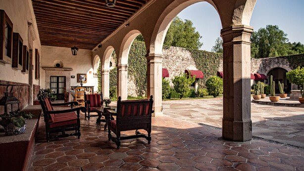 A covered patio with hexagonal stone flooring, wooden furniture, and arches.