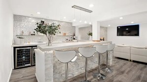 A modern kitchen with a marble countertop, three bar stools, and a built-in wine cooler.