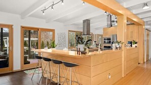 A modern kitchen with a central island, bar stools, and a view of the outdoors through large sliding doors.