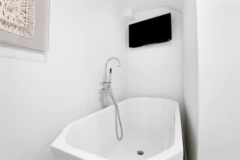 Une baignoire blanche avec un pommeau de douche à main, placée dans un coin de la pièce.