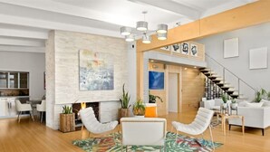 A modern living room with a fireplace, white furniture, and a staircase leading to an upper level.