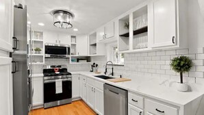 A modern kitchen with white cabinetry, stainless steel appliances, and a wooden floor.