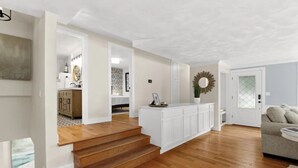 A spacious living area with a wooden staircase, a white entertainment unit, and a gray sofa.