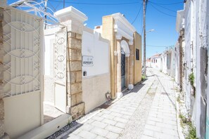 Une rue étroite, bordée de bâtiments des deux côtés, une entrée fermée par un portail et un ciel bleu dégagé.