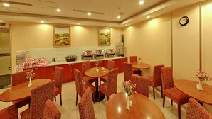 Comedor de hotel con varias mesas redondas y sillas, una barra de cocina con electrodomésticos y dos cuadros con paisajes en la pared.