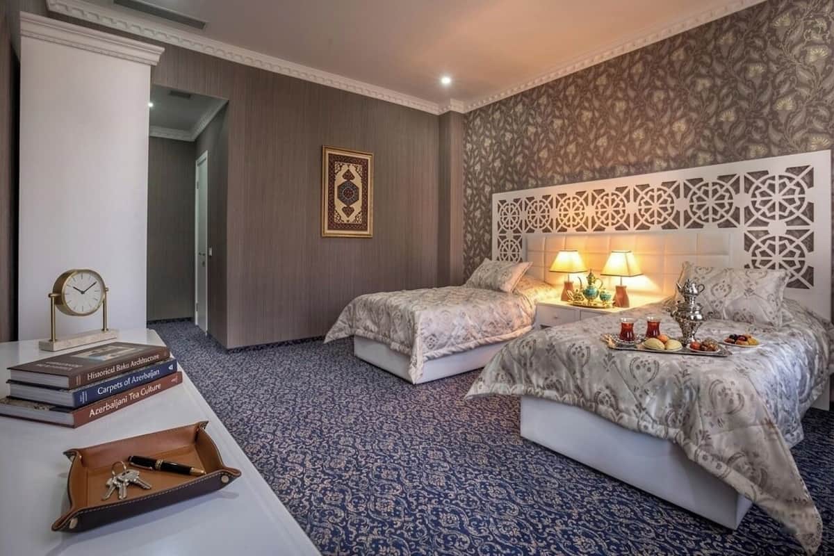 Camera d'albergo con due letti, un comodino, una lampada, un pannello decorativo e un vassoio con cibo.