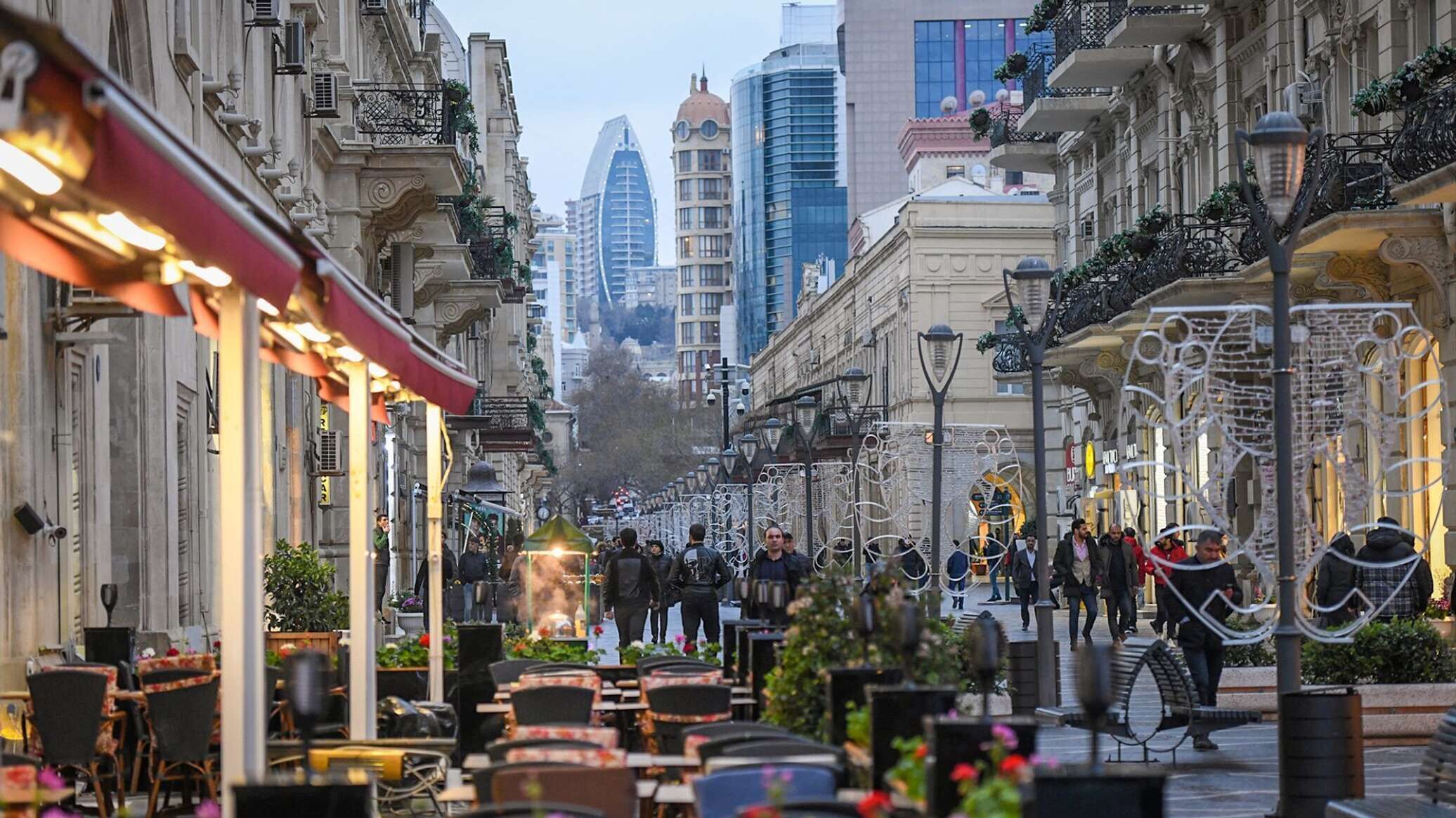 A street lined with cafes and outdoor seating, with pedestrians walking on the sidewalk.