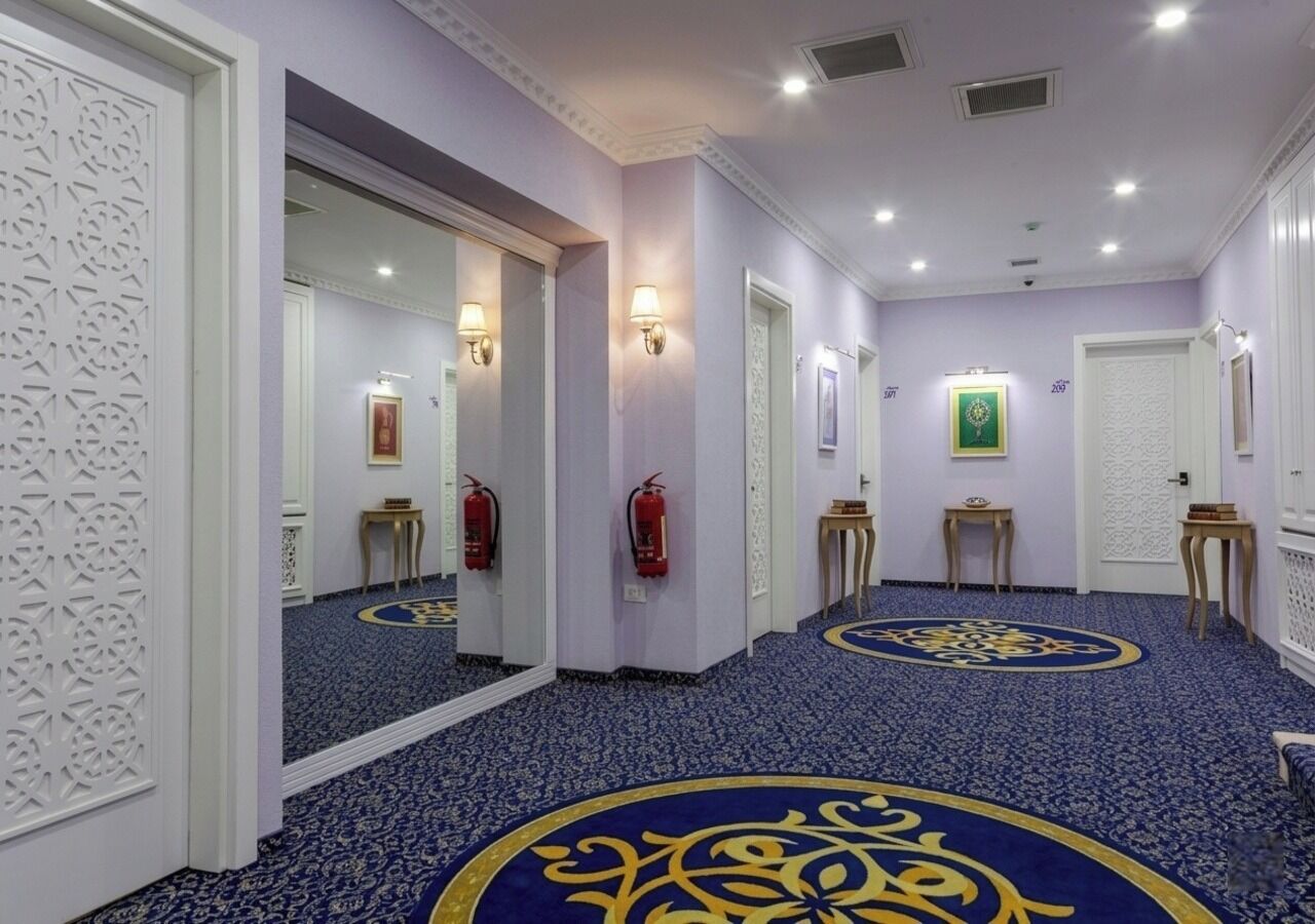 Un pasillo con alfombra azul, paredes blancas y un espejo que refleja la habitación.