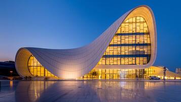 A modern, curved building with large windows and a spacious plaza in front.
