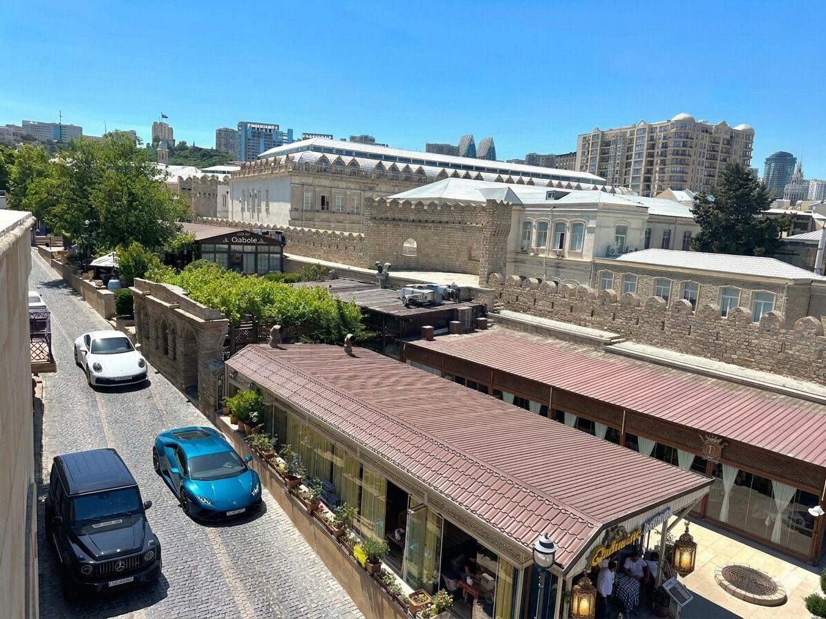 A street view with a building featuring a red roof, a restaurant with outdoor seating, and parked cars.