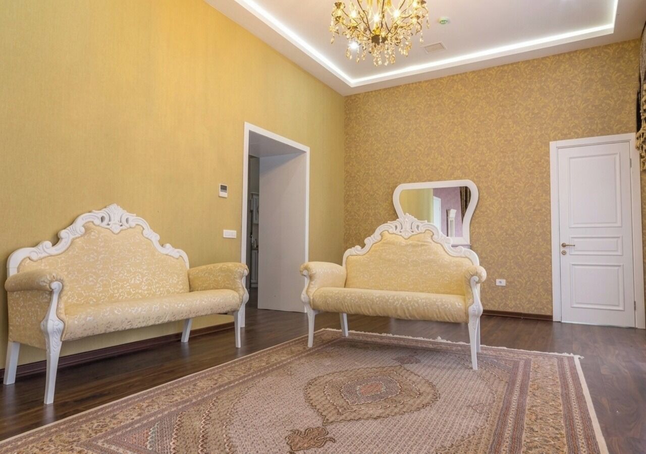 A room with two ornate sofas, a patterned rug, a chandelier, and a door.
