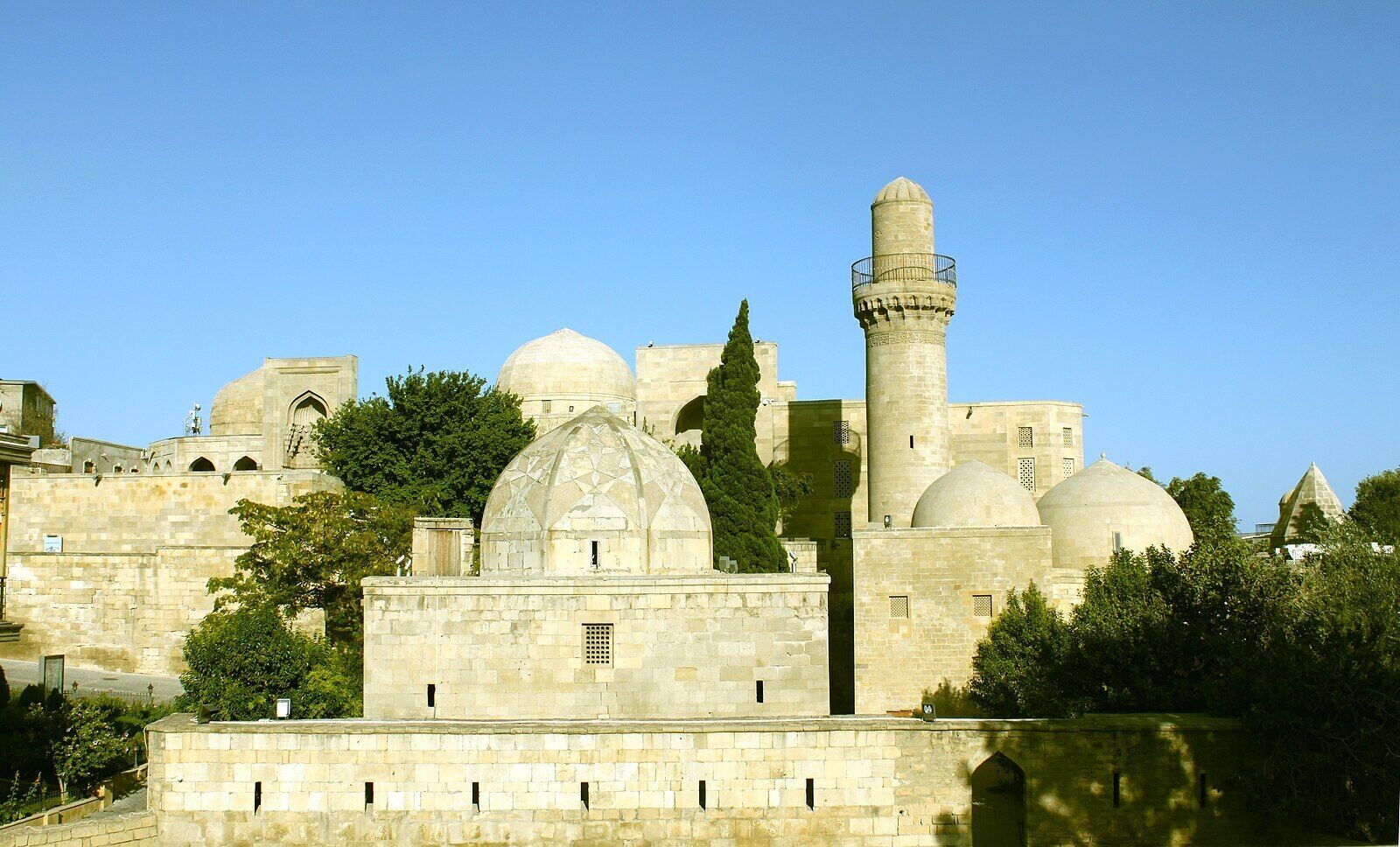 A historic building with multiple domes and a tall minaret, surrounded by greenery.