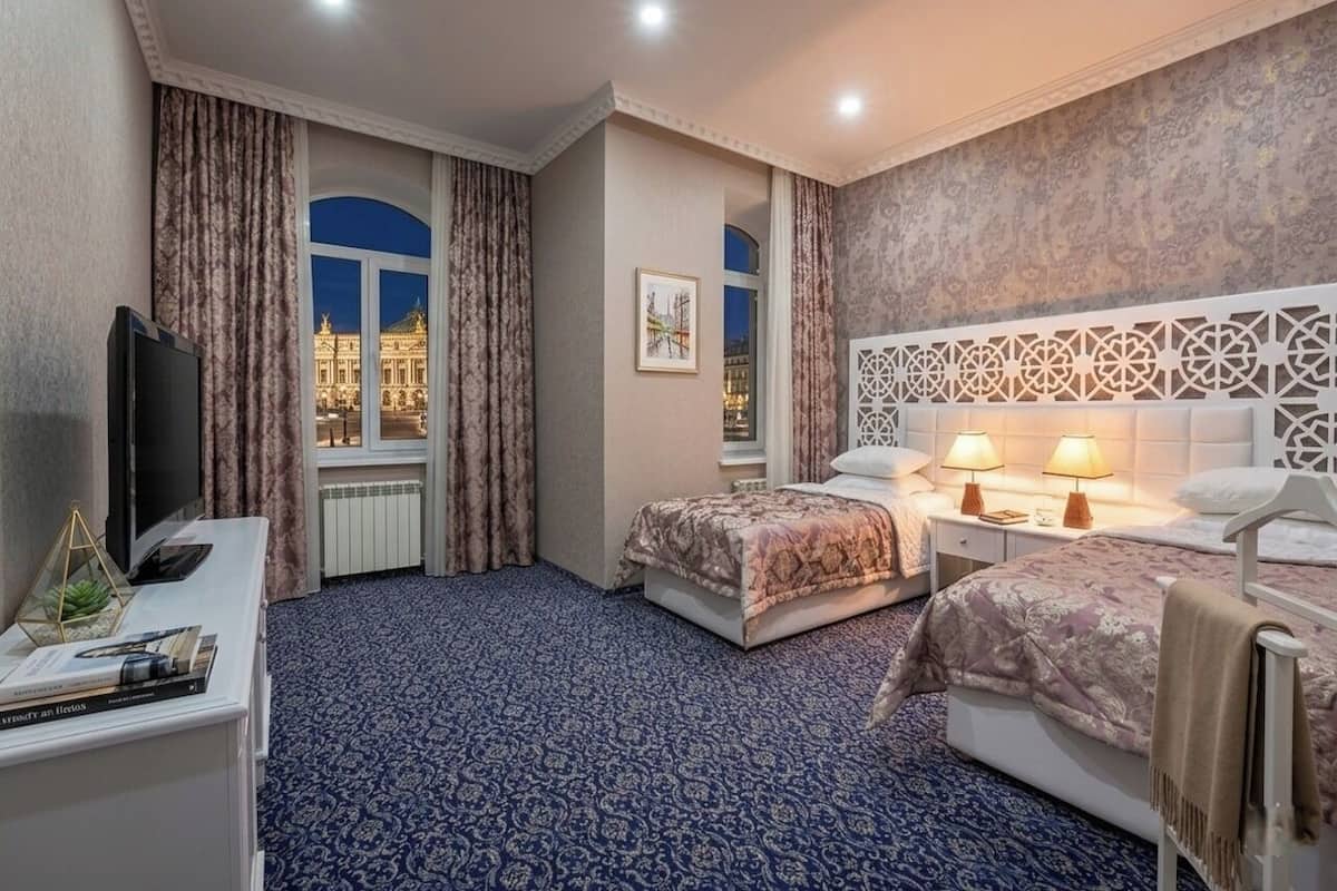 Una camera d'albergo con due letti, una TV, una scrivania e vista su un edificio.