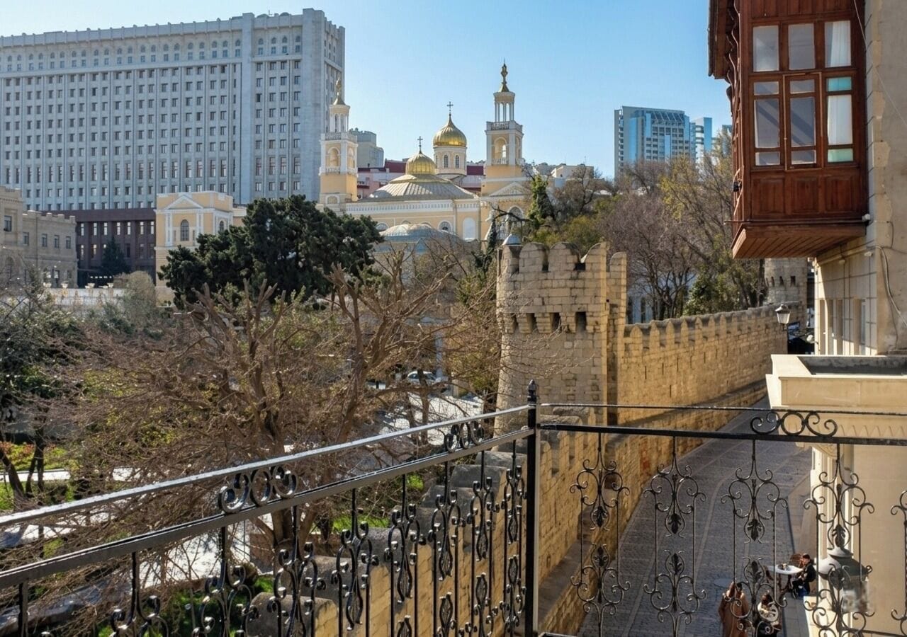 Vista de un paisaje urbano con un edificio destacado que presenta una gran cúpula y un campanario, un muro de piedra y un moderno rascacielos al fondo.