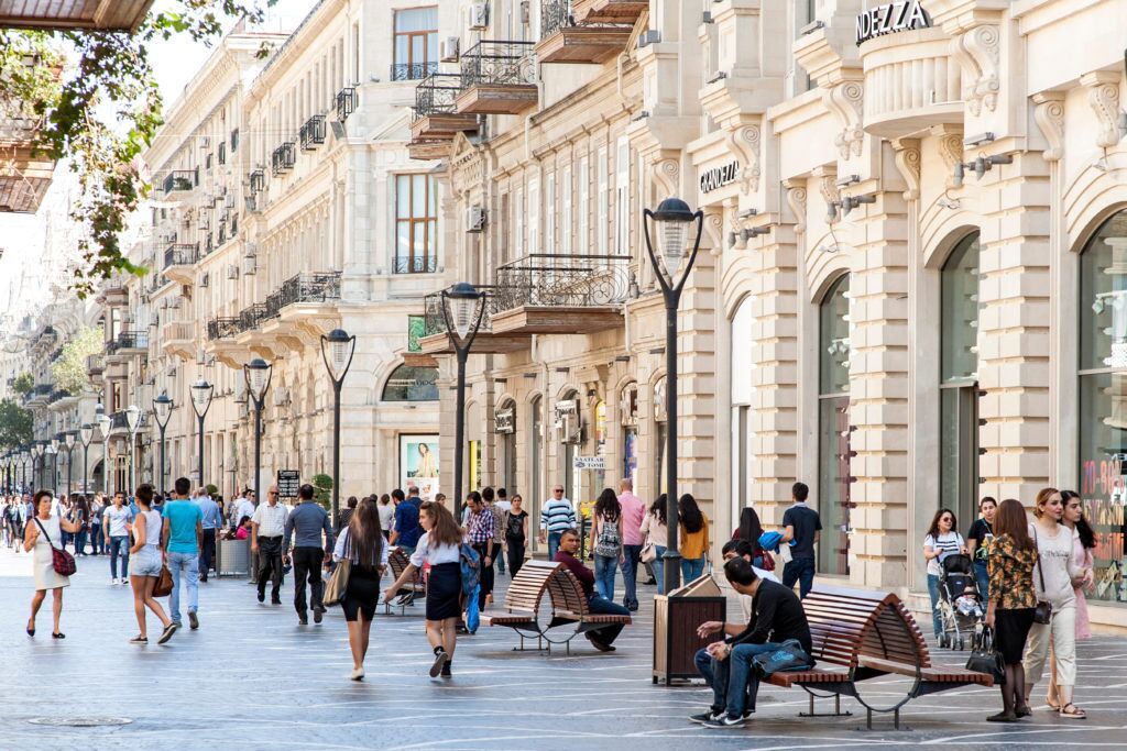 Una concurrida calle urbana con peatones, bancos y edificios históricos.