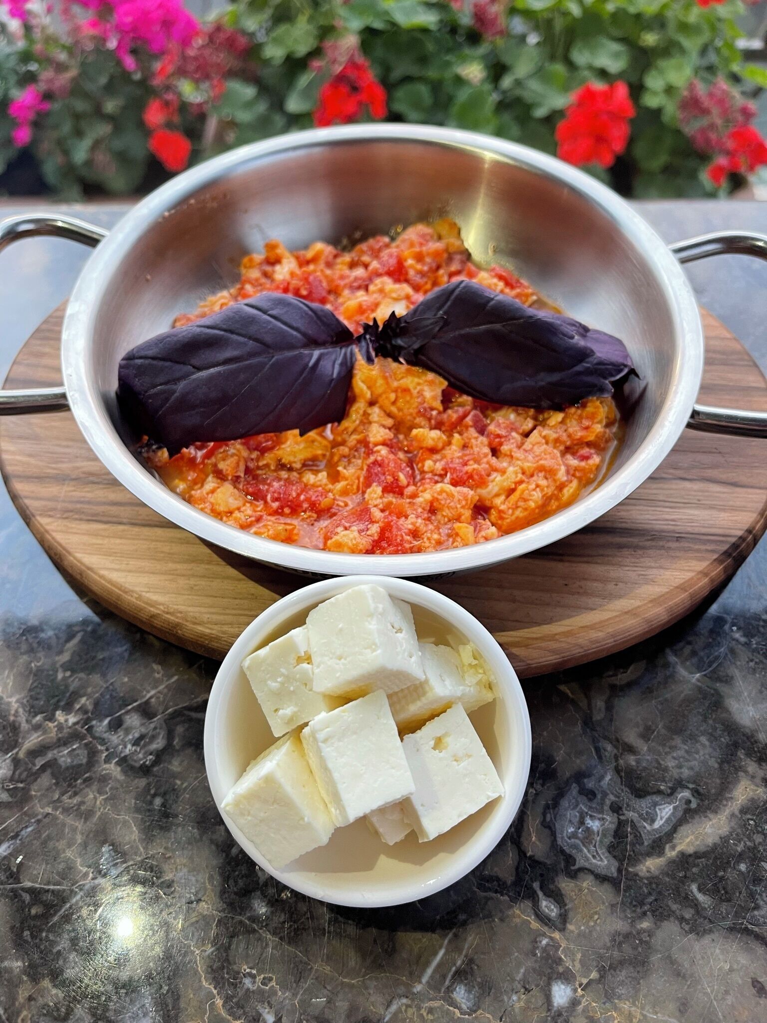 A bowl of tomato-based dish with basil leaves on top, placed on a wooden board.