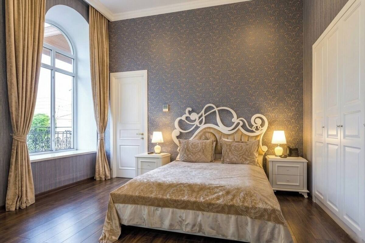 Una camera da letto con un letto grande, due comodini con lampade, una testiera decorativa e una finestra con tende.