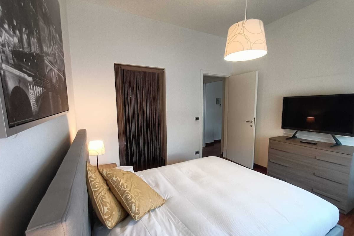 A bedroom with a bed, a television on a dresser, a door, and a wall-mounted picture.