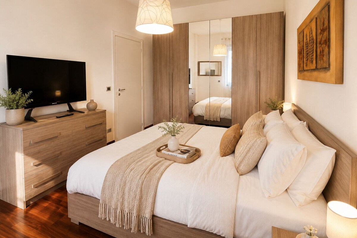 Une chambre moderne dotée d’un téléviseur à écran plat, de meubles en bois, d’un grand lit avec de nombreux oreillers, d’une table de chevet et d’un miroir.
