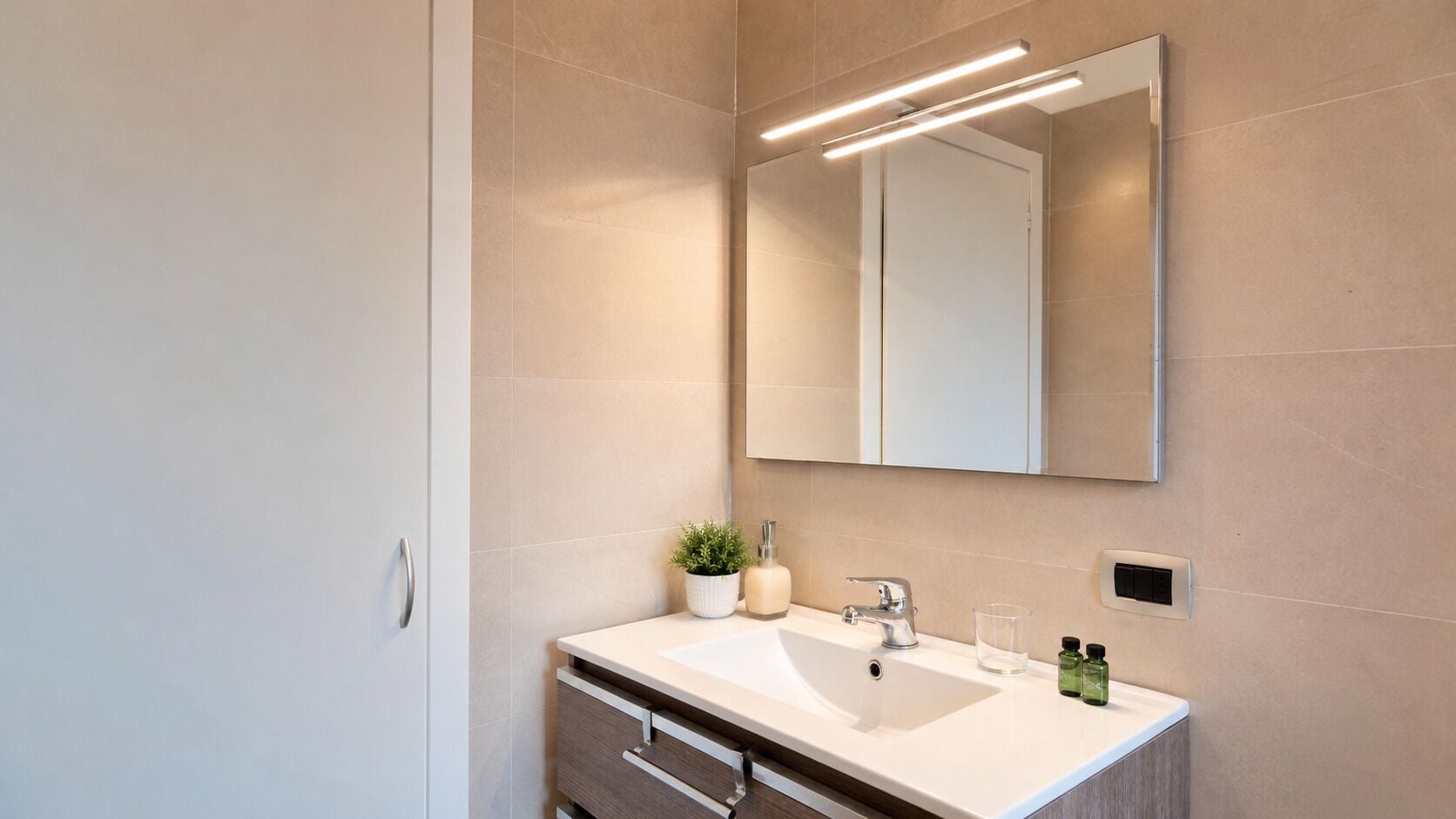 Un baño moderno con un espejo grande, un lavamanos y una planta en maceta.