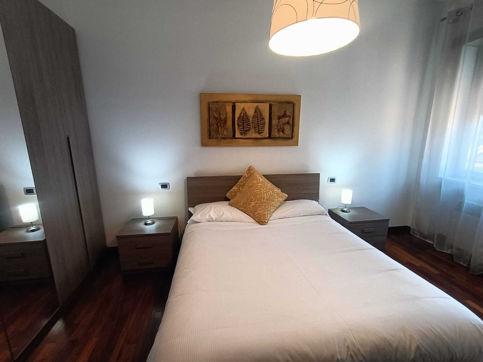 Une chambre d’hôtel avec un grand lit, deux tables de chevet avec des lampes, une tête de lit en bois et une œuvre d’art accrochée au mur au-dessus du lit.