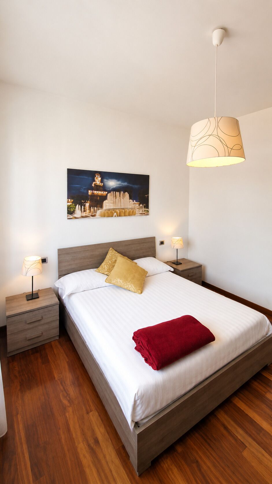 Ein Schlafzimmer mit einem Bett, zwei Nachttischen, einer Wandlampe und einem an der Wand hängenden Bild.