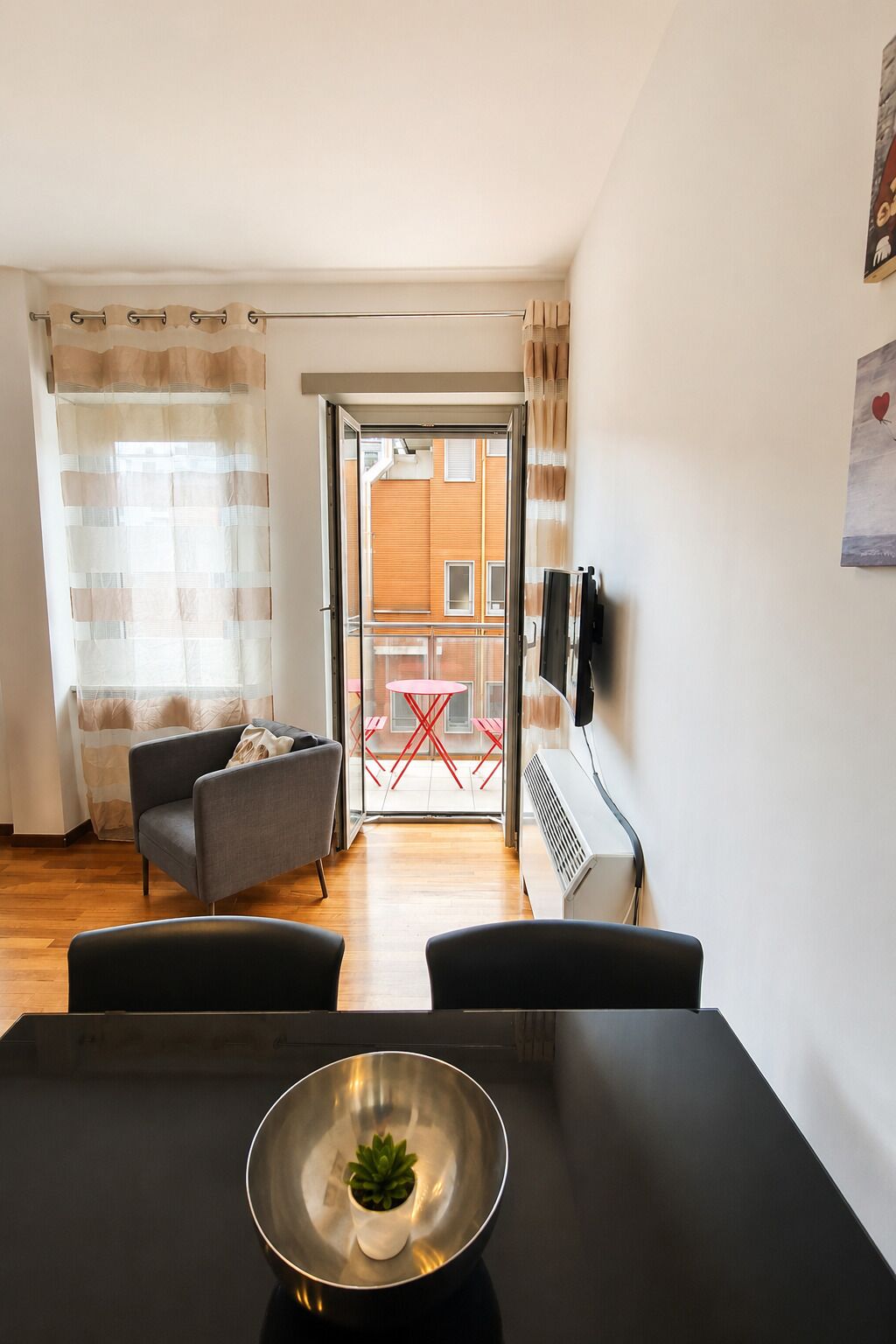 Egy modern nappali, amelyben étkezőasztal, kanapé található, és kilátás nyílik egy kültéri területre, ahol piros asztal és székek állnak.