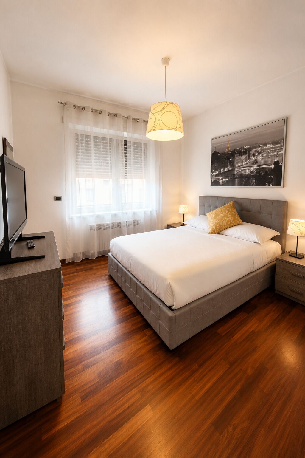 Un dormitorio moderno con una cama, mesitas de noche, un televisor y un cuadro de un paisaje urbano.