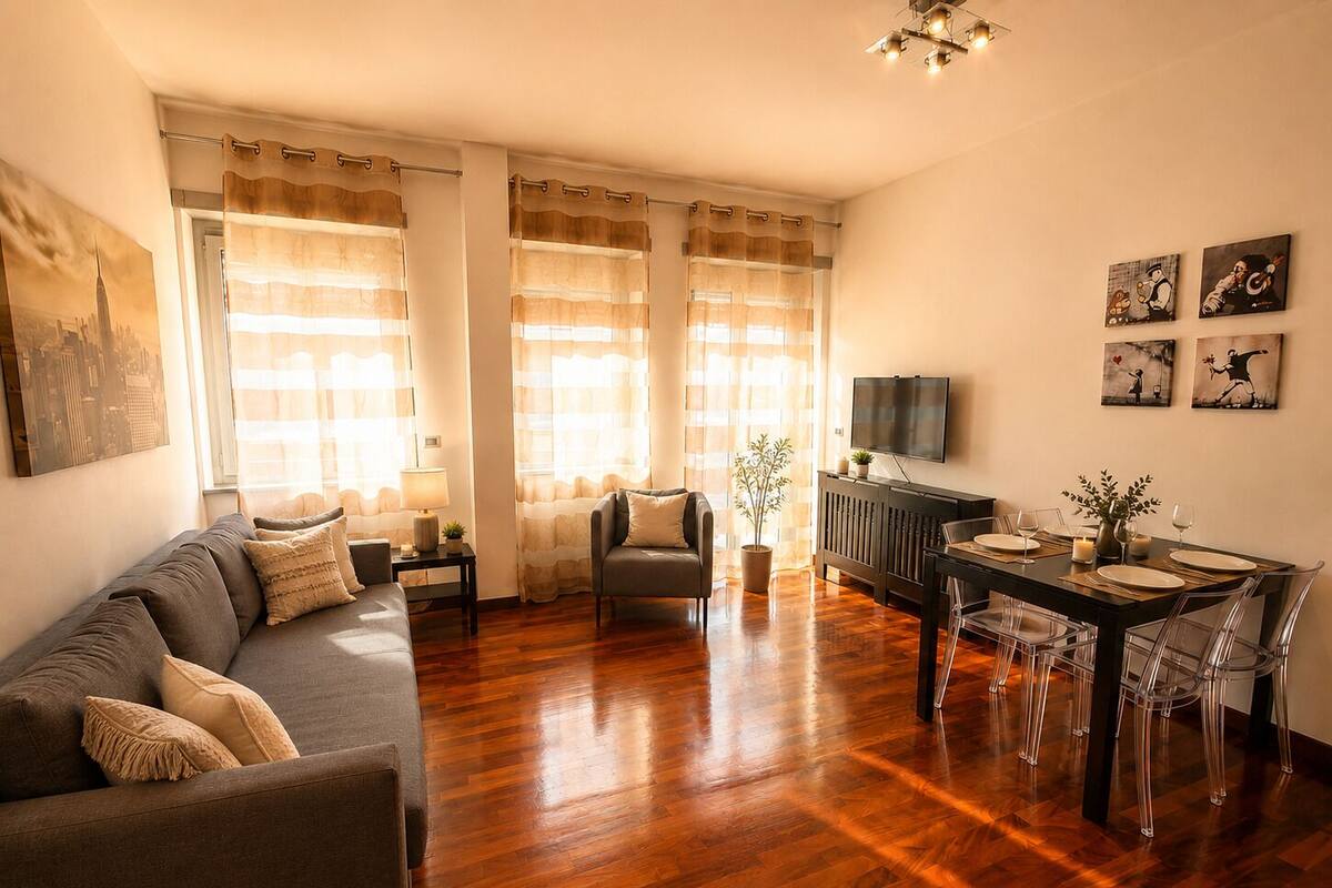 A living room with a sofa, a dining table with chairs, a TV, and artwork on the wall.