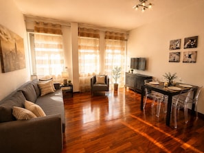 Uma sala de estar com sofá, mesa de jantar com cadeiras, televisão e obras de arte na parede.