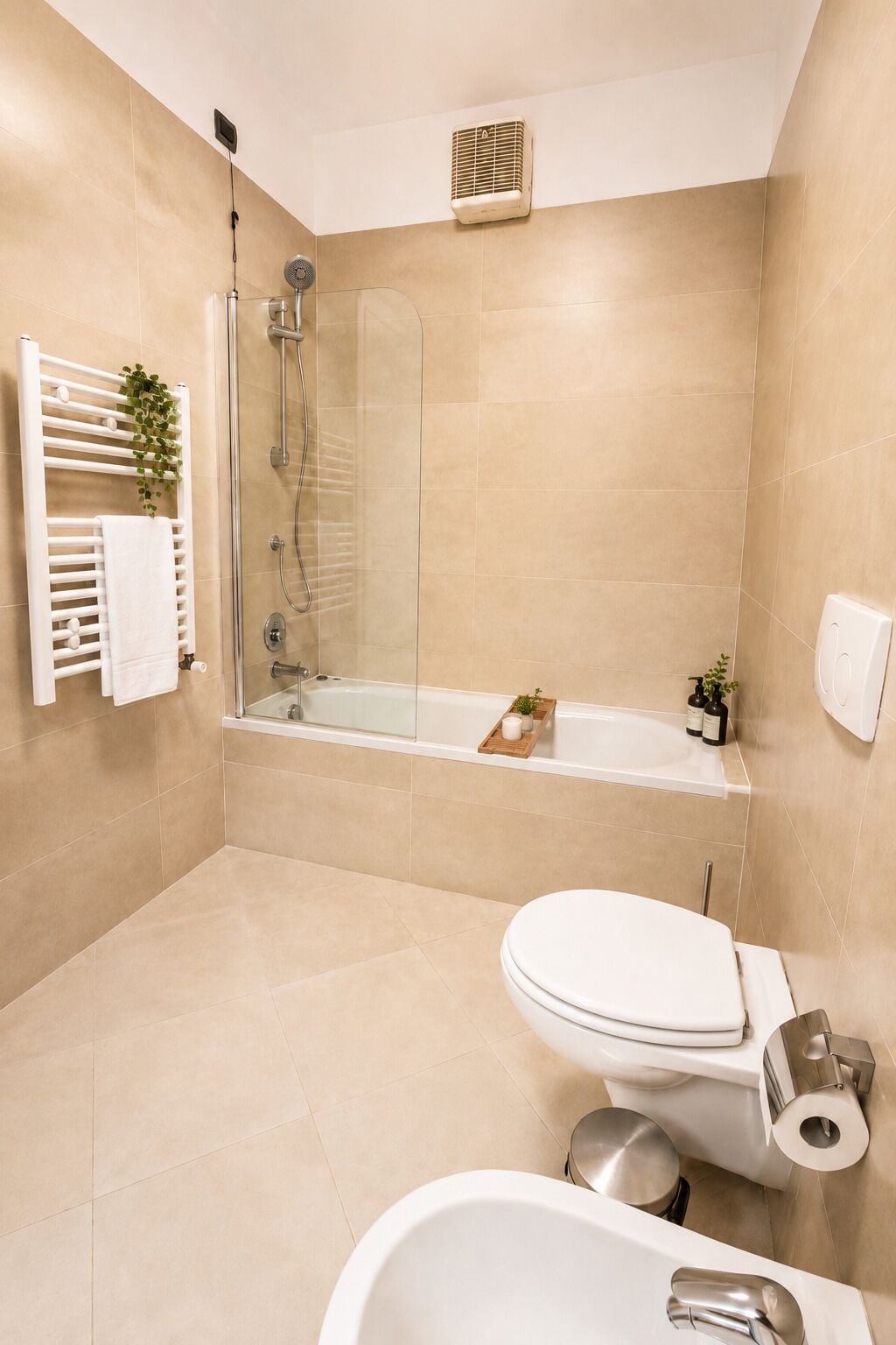 A modern bathroom with a glass-enclosed shower, a bathtub, a toilet, and a towel rack with a plant.