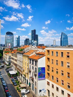 A cityscape with modern and historic buildings, a clear sky, and a street with parked cars. - Style Homes Brera (Milan)