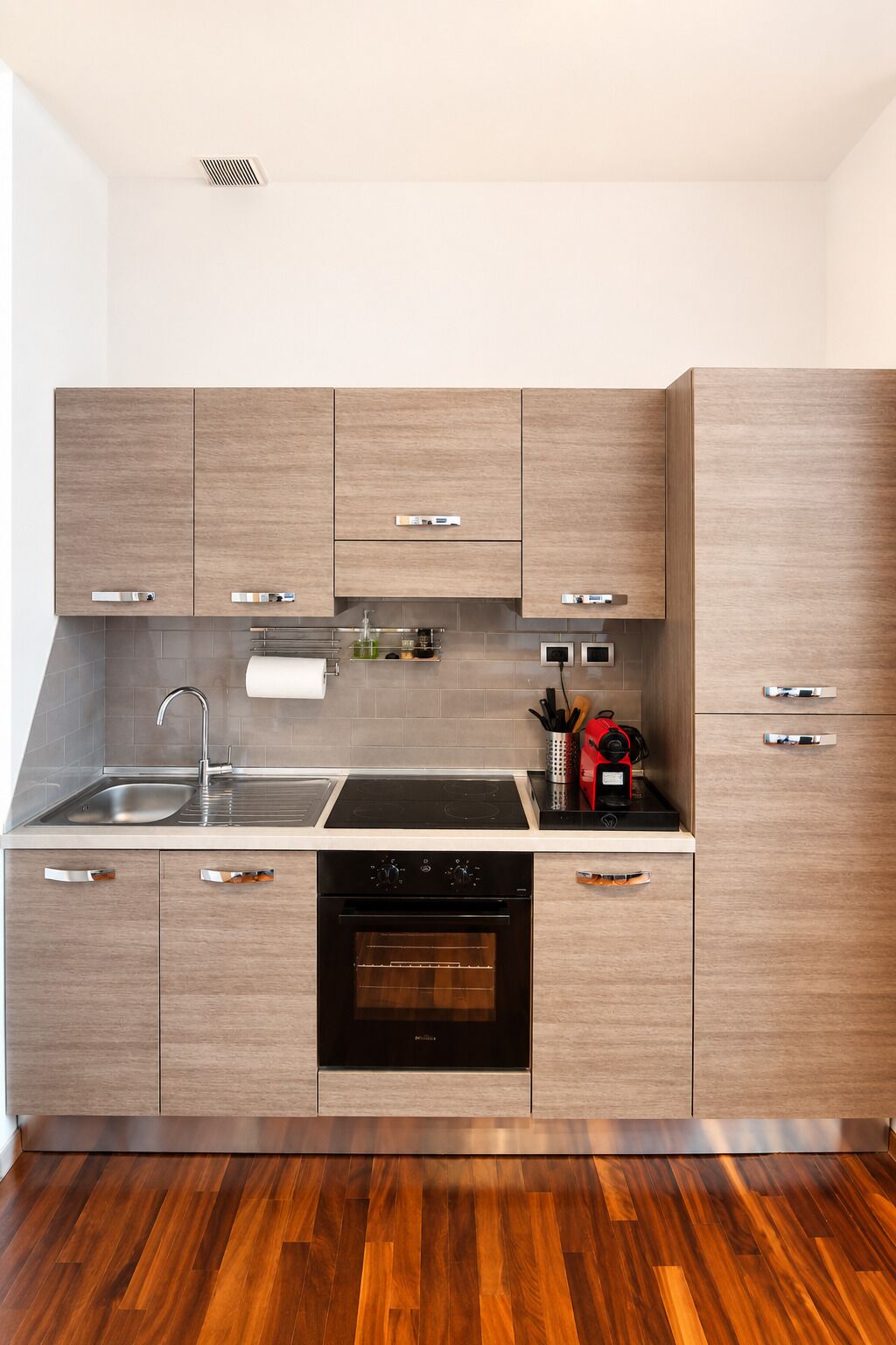 A modern kitchen with wooden cabinets, a stainless steel sink, a built-in oven, and a black dishwasher.