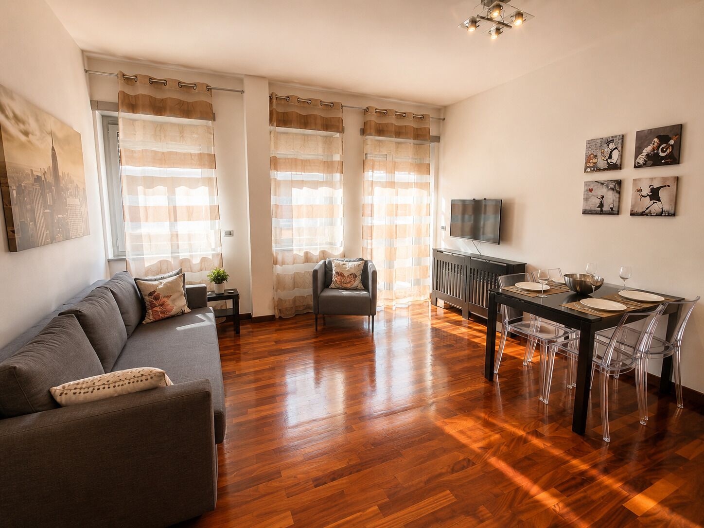 A living room with a sofa, a dining table with chairs, a TV, and artwork on the wall.