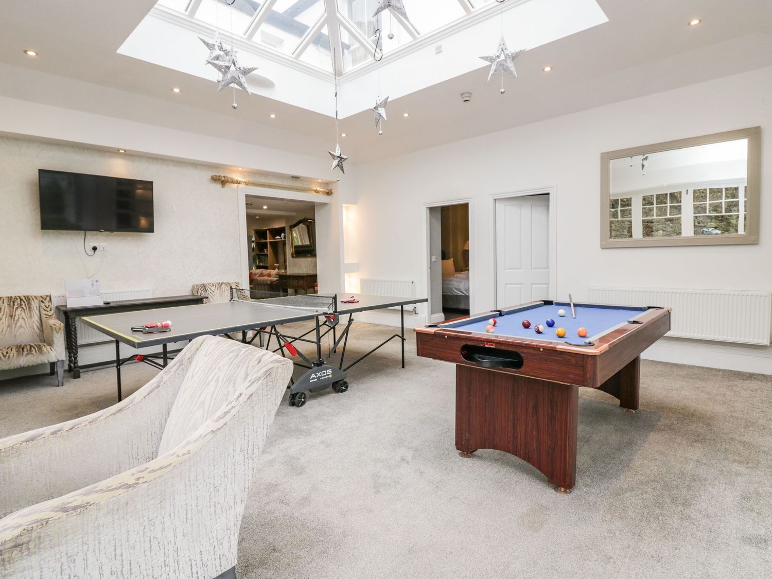 A spacious room with a pool table, a billiards table, a comfortable chair, and a television.