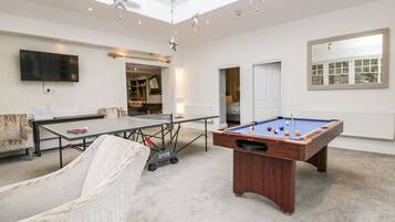 A spacious room with a pool table, a billiards table, a comfortable chair, and a television.