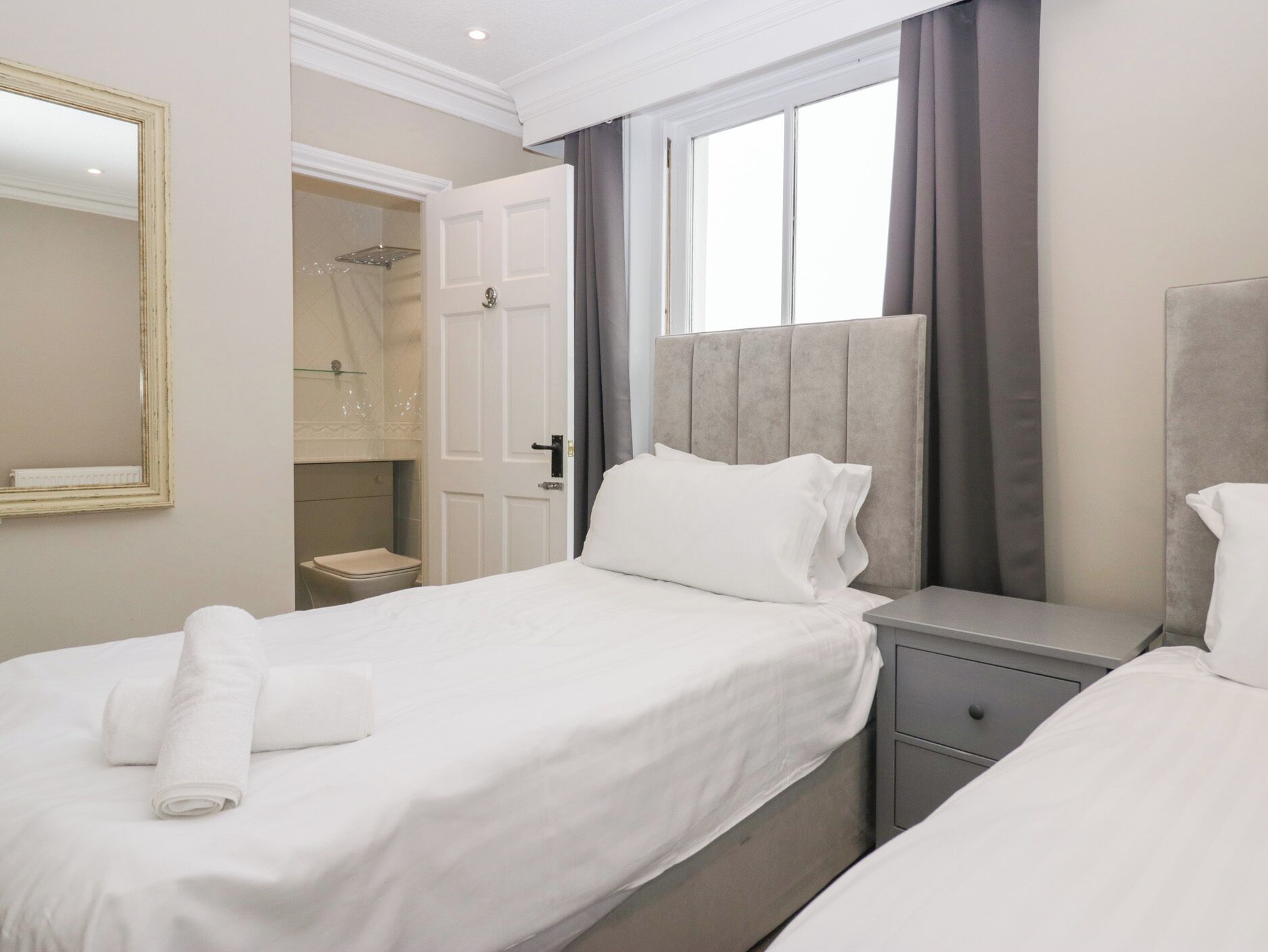 Une chambre d’hôtel comprenant un lit, une table de chevet, un miroir, une fenêtre avec des rideaux et un espace douche.