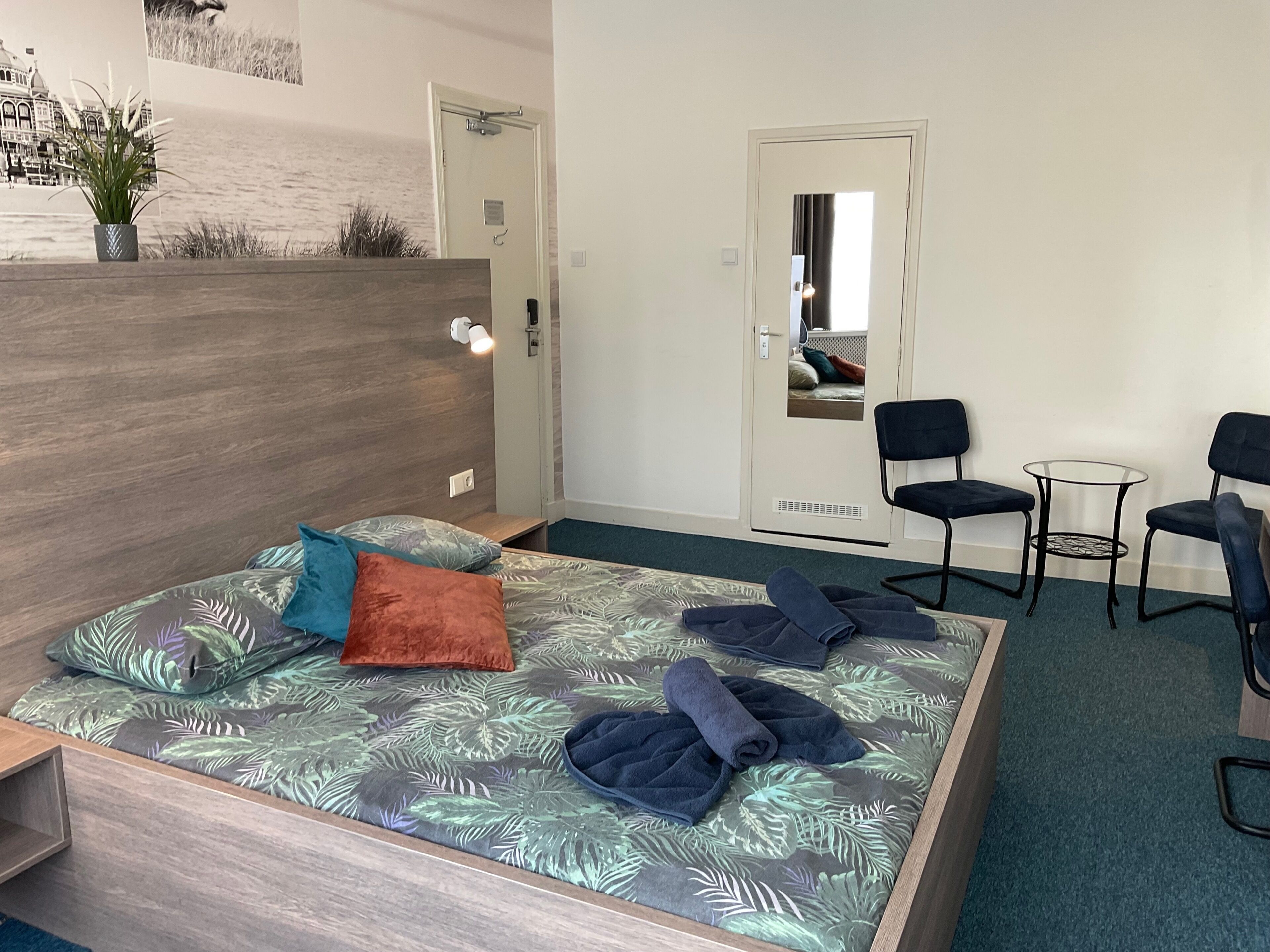 Ein Zimmer mit einem Bett, zwei Stühlen, einem kleinen Tisch und einer Tür.