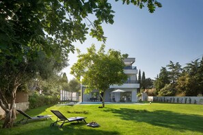 Une maison moderne avec une piscine, un arbre et deux chaises longues dans le jardin.